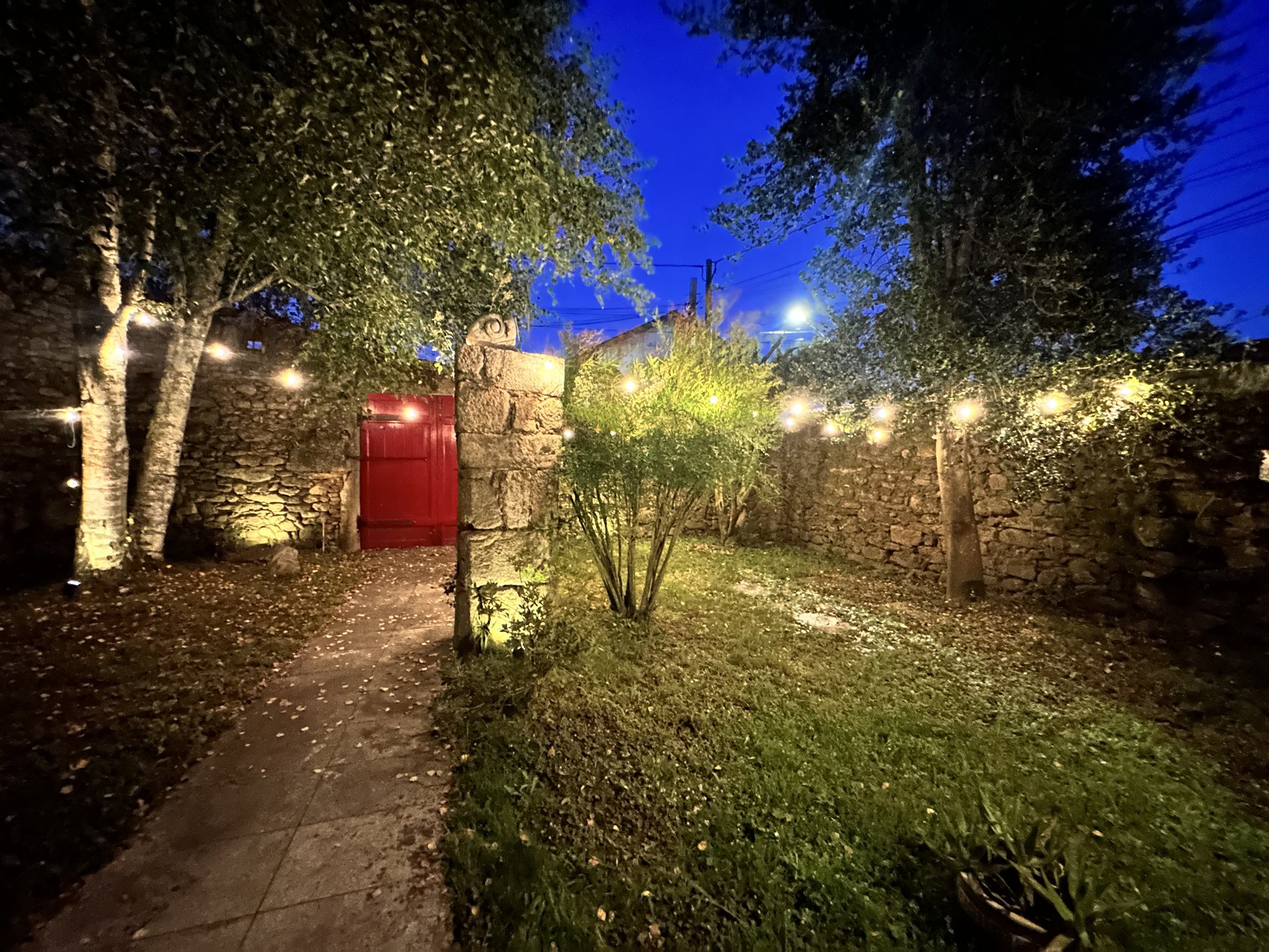 El portalón rojo de Casa do Bidueiro de noche — patio de casa rural gallega